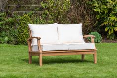 two white pillows sit on top of a wooden bench in the grass near some bushes