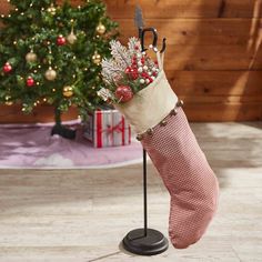 a christmas stocking with an umbrella and flowers is on a stand in front of a christmas tree