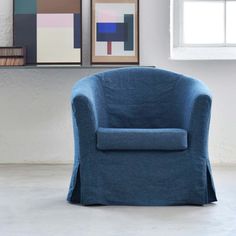 a blue chair sitting in front of a window next to a painting on the wall