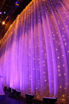 a stage with purple lights and white drapes on the wall behind it is set up for a wedding ceremony