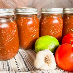 tomatoes, limes and garlic sit in front of jars filled with tomato relish