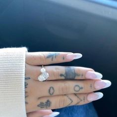 a woman's hand with tattoos and a diamond ring on her left thumb, in the car