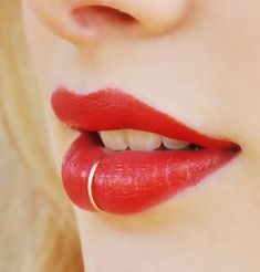 a woman with red lipstick and gold ring on her lip, closeup shot from the neck down