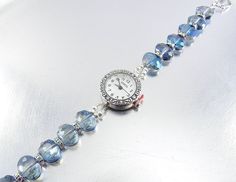 "A gorgeous addition to your jewelry collection, I made this elegant and functional bracelet watch with 9x12mm faceted blue luster glass, silver aurora borealis wheel spacers and silver plated findings. Super cool fold-over magnetic clasp makes for an easy on and off of your wrist. This round, Geneva watch face has a scroll detail, and measures about 22mm. It has a stainless steel back and is water resistant. **SIZING - I offer this watch for wrists sized 5 1/2\" through 8 1/2\". SELECT the size Adjustable Sapphire Crystal Jewelry, Round Crystal Watch As Gift, Silver Beaded Stainless Steel Jewelry, Crystal Watch As A Gift, Blue Stainless Steel Jewelry With Round Dial, Blue Stainless Steel Round Dial Jewelry, Elegant Crystal Watches As Gifts, Elegant Crystal Watches For Gifts, Adjustable Silver Bracelet Strap Jewelry And Watches