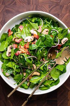 a salad with spinach, mushrooms and bacon in a white bowl on a wooden table