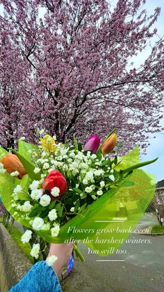 a person holding a bouquet of flowers in front of a tree with pink and yellow flowers