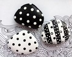 three black and white painted rocks sitting on top of a flowered tablecloth with flowers