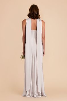 the back of a woman wearing a white dress with a long vest over her shoulders