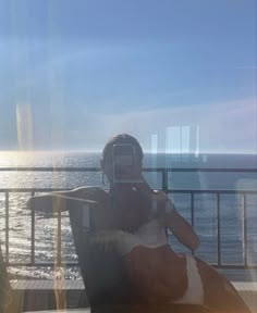 a woman taking a photo with her cell phone while sitting on a deck overlooking the ocean