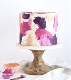 a white cake with pink and purple icing on it next to a bowl of flowers