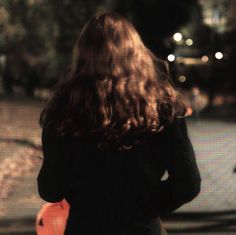 a woman walking down the street at night with her back to the camera and long hair blowing in the wind