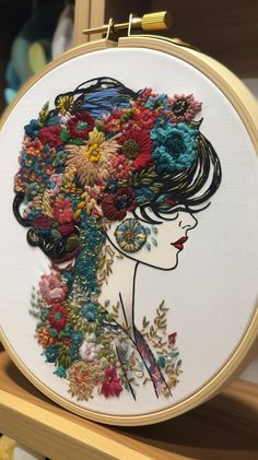 a woman's head with flowers in her hair is embroidered onto a white hoop