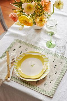 a white table with yellow and green plates, silverware and flowers in vases