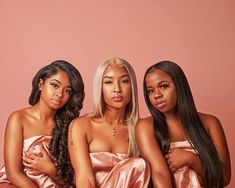 three women in pink satin robes sitting on a couch with their arms around each other