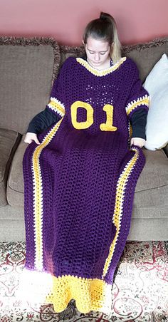 a woman sitting on a couch wearing a purple crocheted blanket with the number ten on it