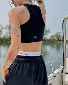 a woman with tattoos on her arm standing next to a boat and holding onto a pole