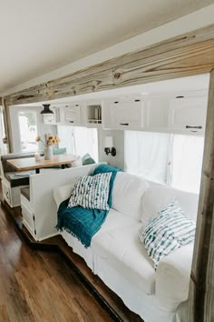 a living room with white couches and wooden flooring in front of a kitchen