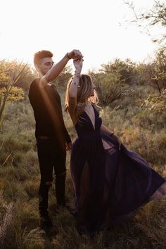 a young man and woman standing in the grass with their arms around each other as they hold hands