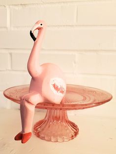 a pink flamingo figurine sitting on top of a glass cake plate