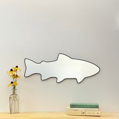 a fish shaped mirror sitting on top of a wooden table next to a vase with flowers