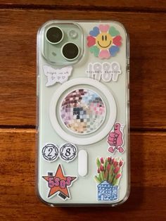 an iphone case with stickers on it sitting on top of a wooden table next to a pair of glasses