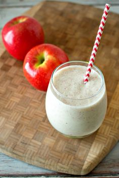 an apple smoothie in a glass next to two apples