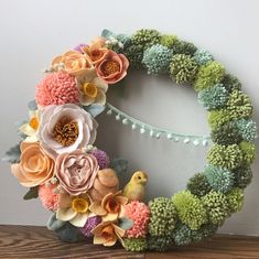 a wreath made out of fake flowers sitting on top of a wooden table next to a wall