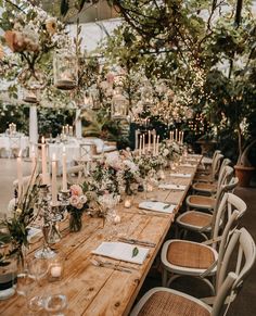 a long wooden table topped with lots of white and pink flowers next to tall candles