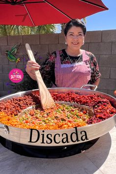 a woman standing in front of a large pan filled with food