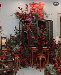 a room filled with lots of red flowers and wooden furniture next to a wall covered in greenery