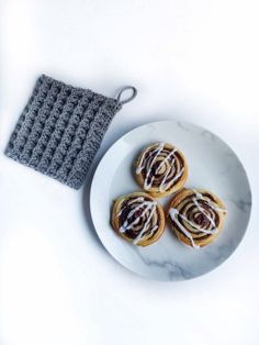 three crocheted pastries on a plate next to a dish towel and napkin