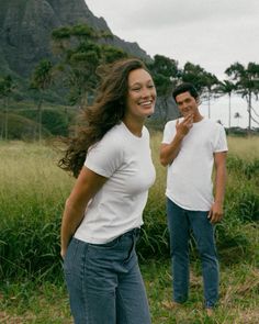 two people are standing in the grass and one is talking on his cell phone while the other looks at him