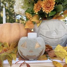 a cement pumpkin shaped candle holder sitting on top of a table next to flowers and candles