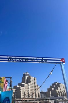 a sign that reads welcome to cuba hanging from the side of a building with buildings in the background