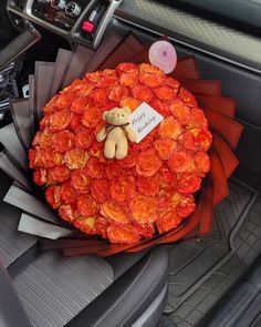 a teddy bear sitting on top of a bouquet of flowers in the back seat of a car