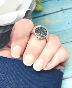 a woman's hand with a ring on her finger and flowers in the background