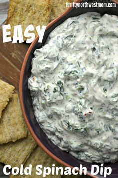 a bowl filled with spinach dip next to tortilla chips on a wooden table