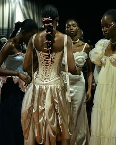 several women in dresses are walking down the catwalk at a fashion show, with one woman wearing a corset on her head