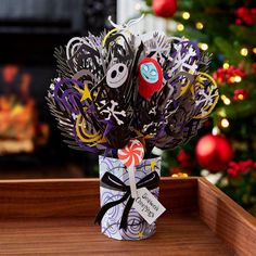 a vase filled with paper and scissors on top of a wooden table next to a christmas tree