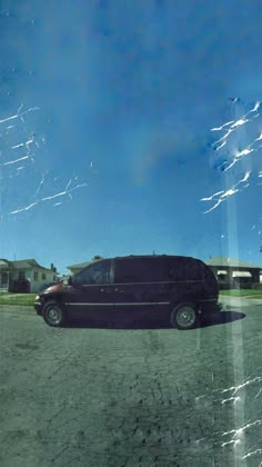 a black van parked in a parking lot next to a house and trees with blue sky