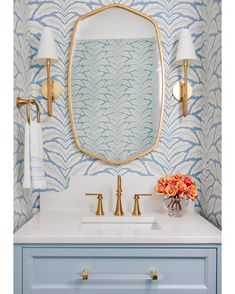 a bathroom with blue and white wallpaper, gold fixtures and a large mirror over the sink