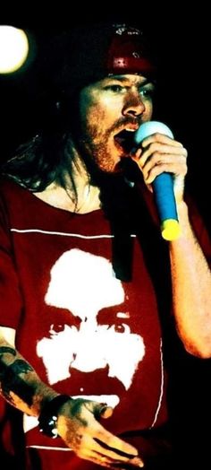 a man with long hair holding a microphone in his hand and wearing a red shirt