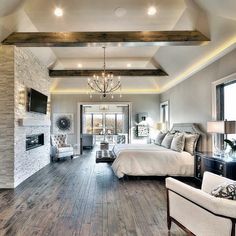 a large bedroom with wood floors and white furniture in front of a stone fireplace mantel