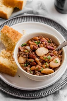 a white bowl filled with beans and bread on top of a plate next to a fork