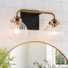 a bathroom light with two clear globes hanging from it's brass finish fixture