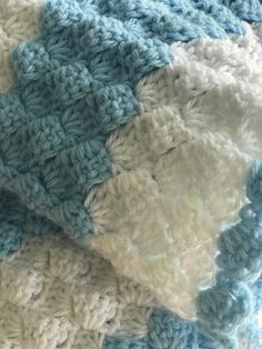 a blue and white crocheted blanket laying on top of a bed