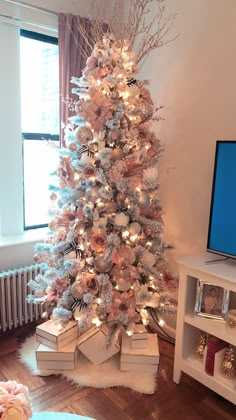 a white christmas tree decorated with pink and silver ornaments in front of a flat screen tv