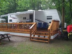 an rv is parked in the woods next to picnic tables and benches with bikes on them