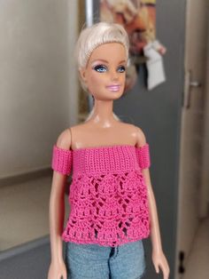 a barbie doll with blonde hair wearing shorts and a pink crochet top in front of a refrigerator