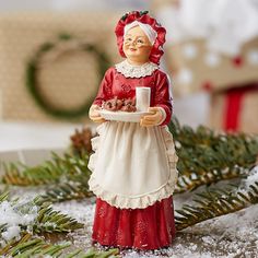 a figurine holding a cup and plate in the snow with pine branches around it